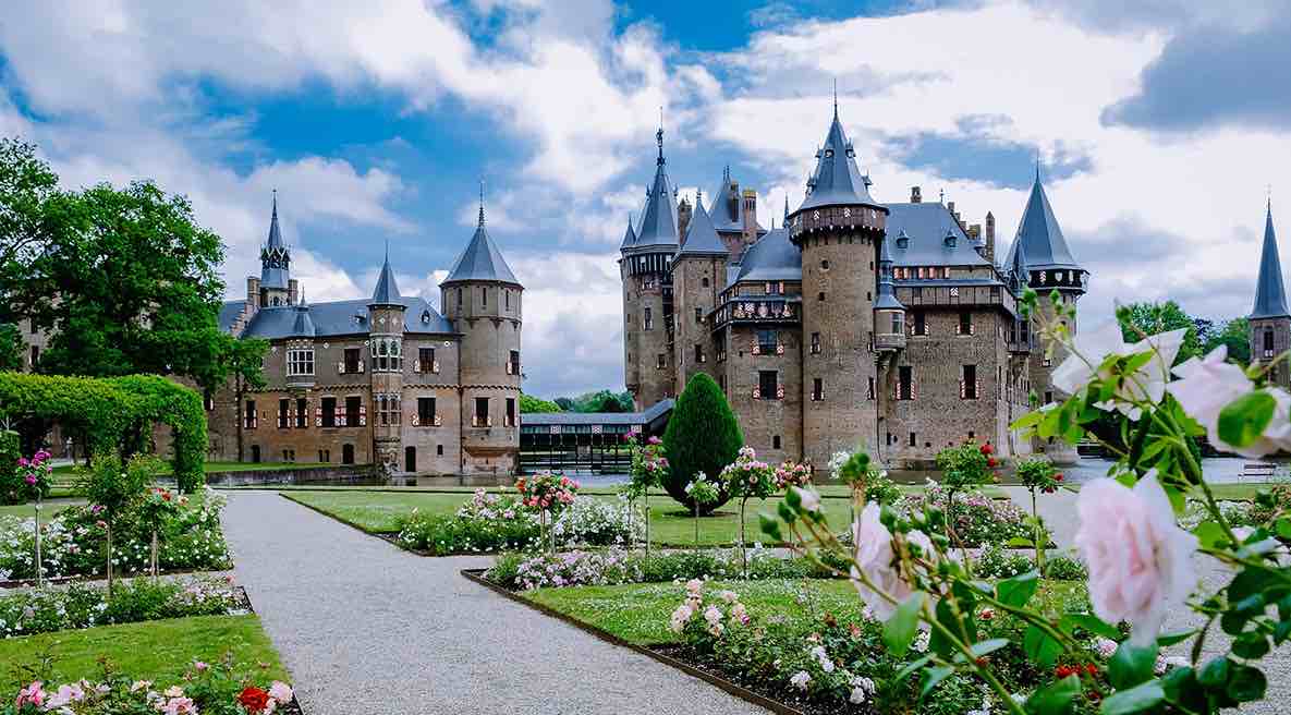 Castillo medieval rodeado de jardines bien cuidados en una ciudad europea.