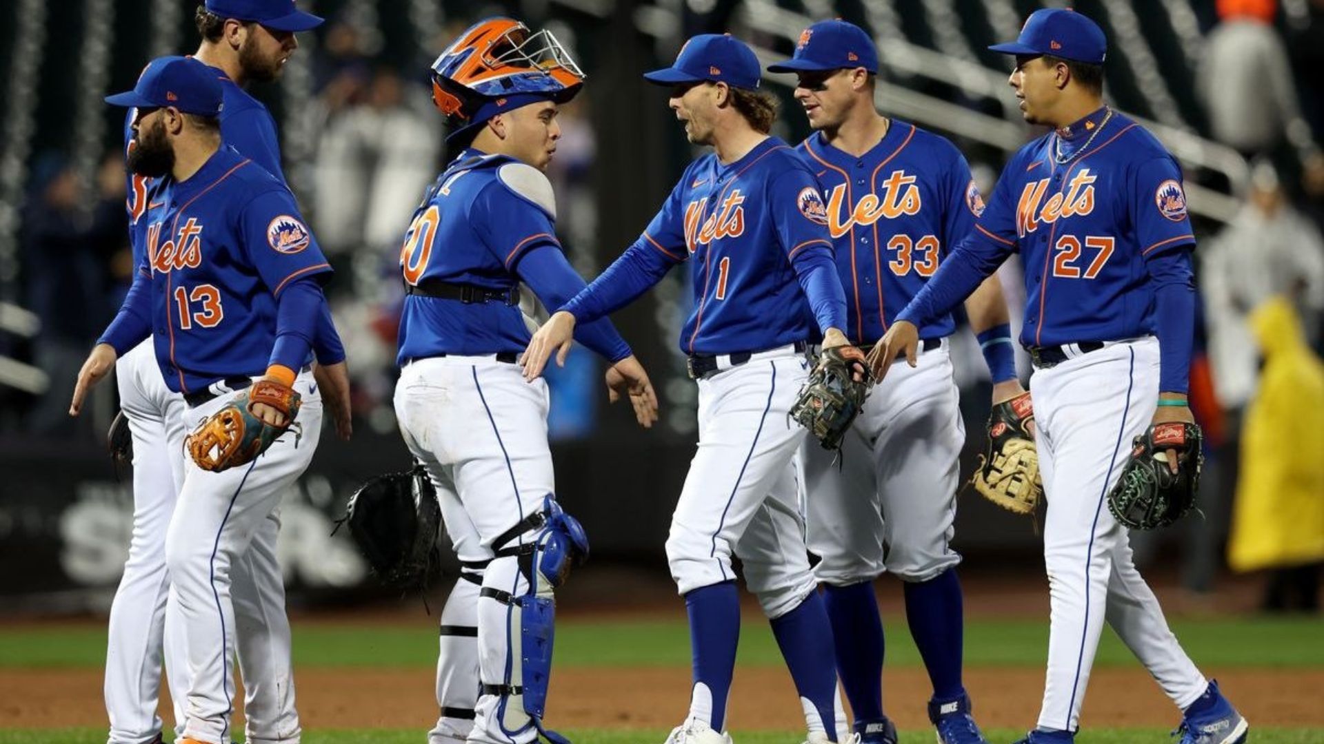 Jugadores de los New York Mets saludando y celebrando al final de un partido, usando el uniforme azul con el logo de los Mets.