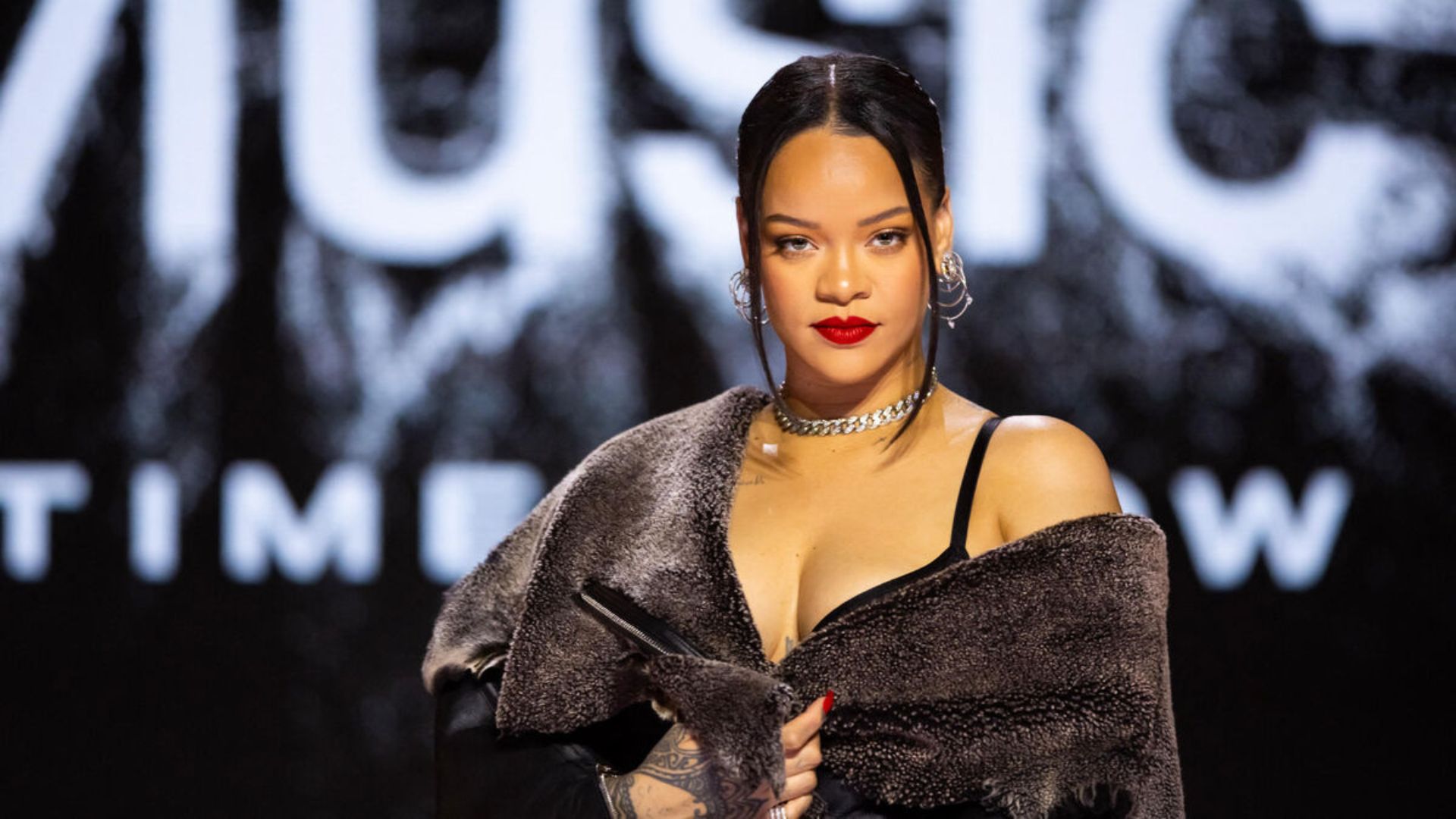 Rihanna durante un evento público, vestida con un conjunto elegante y maquillaje destacado.