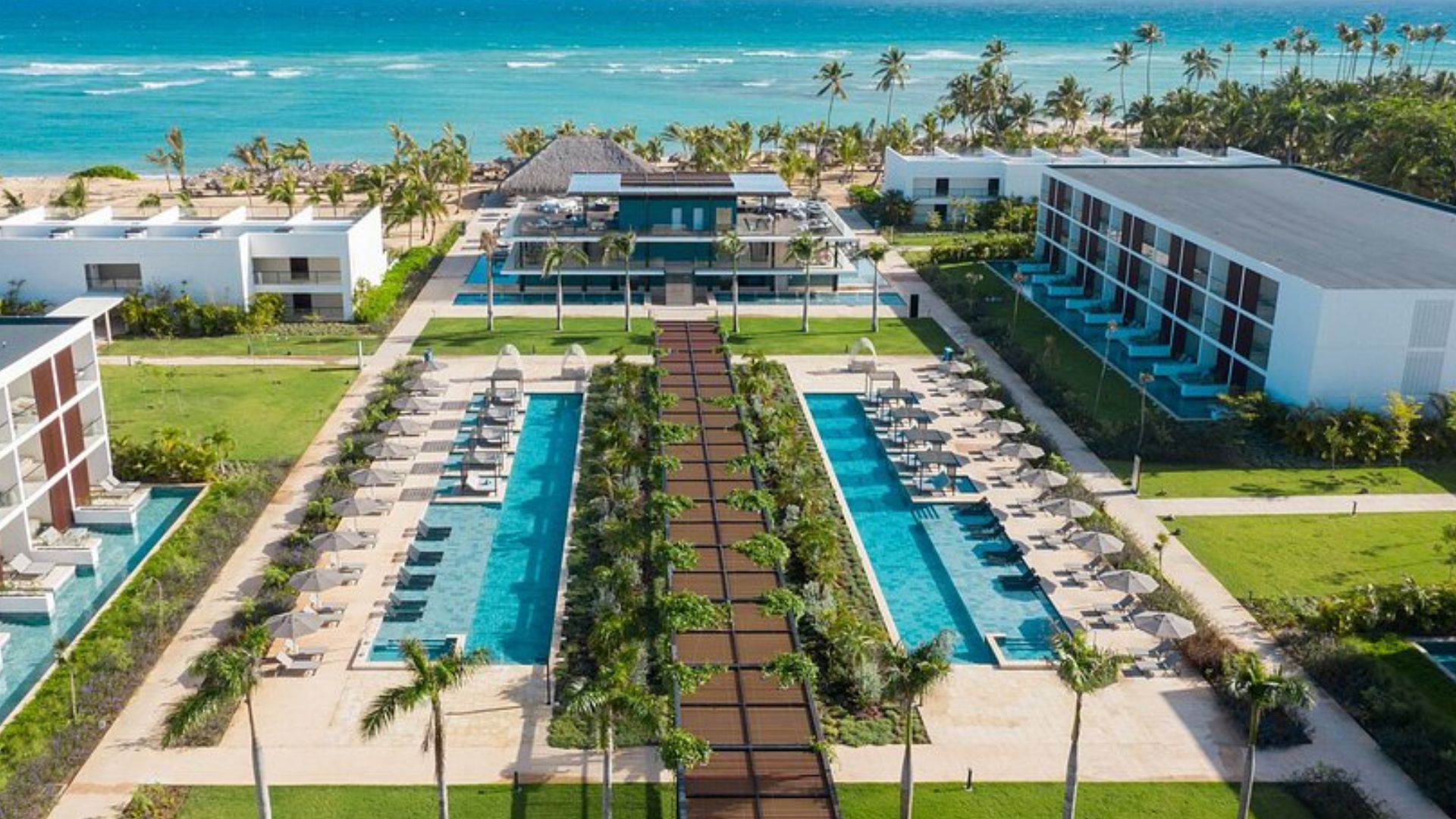 Vista aérea de un resort de lujo frente a la playa en Punta Cana, con piscinas y jardines bien cuidados.