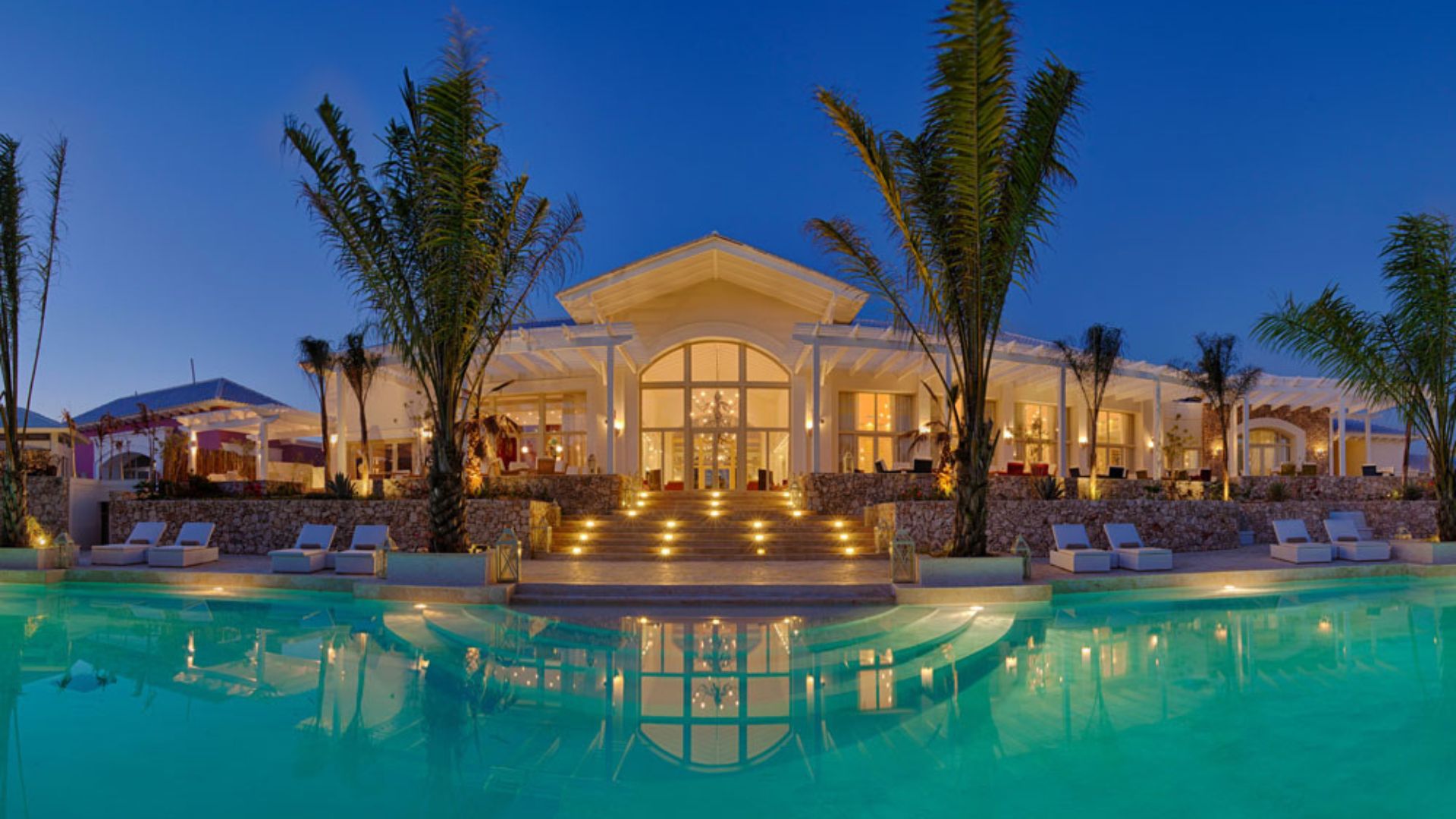 Hotel de lujo en Punta Cana con piscina iluminada, palmeras y arquitectura caribeña al atardecer.