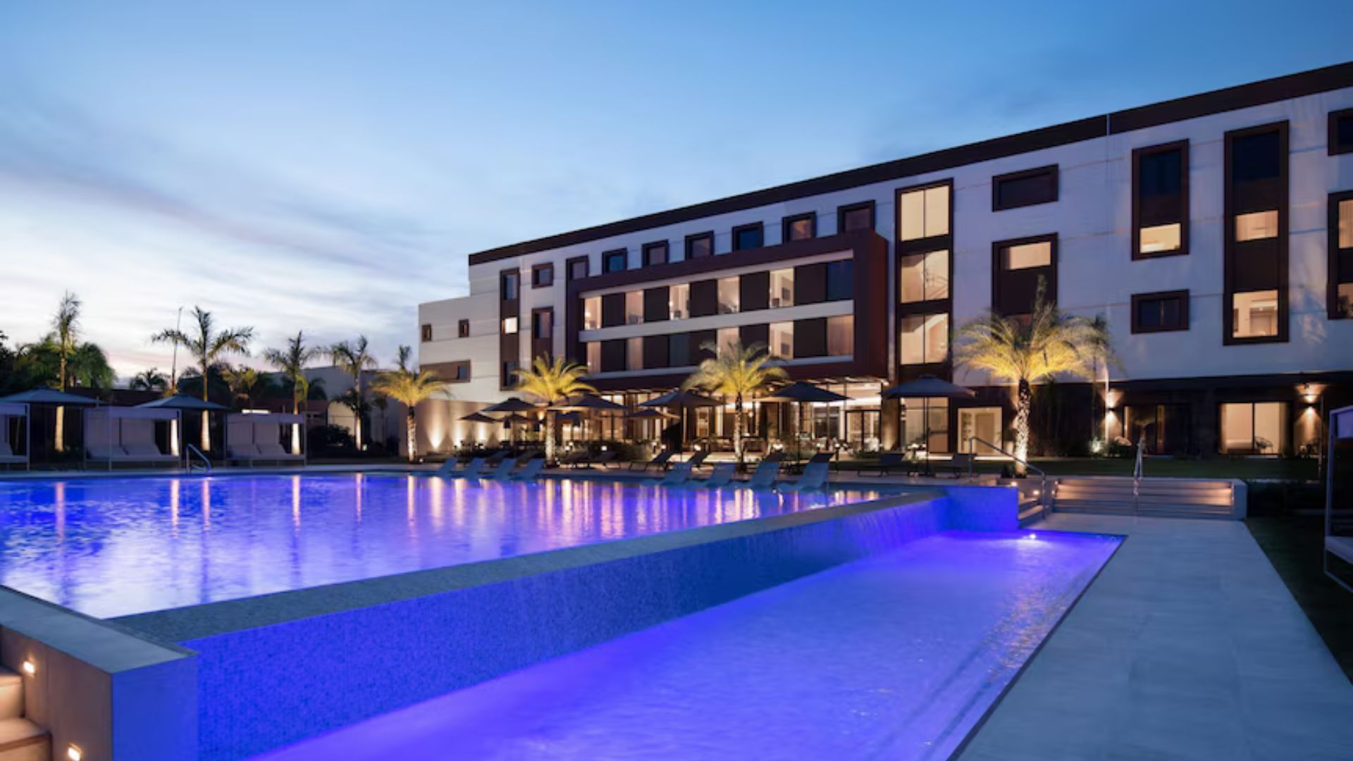 Hotel moderno en Punta Cana con piscina iluminada y áreas de descanso junto a palmeras.