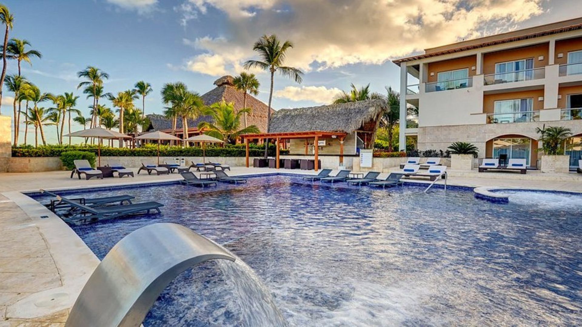 Hotel moderno en Punta Cana con piscina al aire libre, tumbonas y balcones con vista al área común.