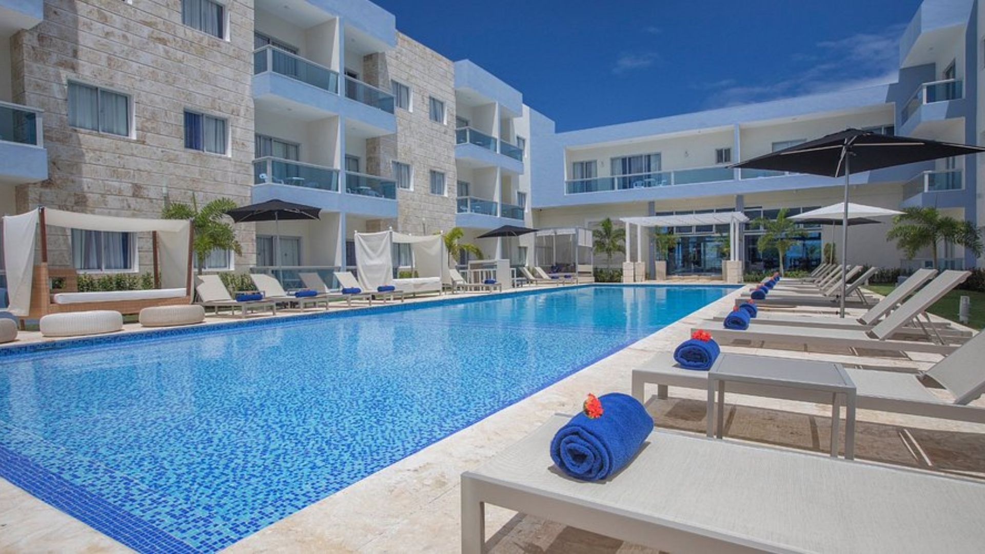 Piscina al aire libre de un hotel en Punta Cana con tumbonas, sombrillas y edificios modernos alrededor.