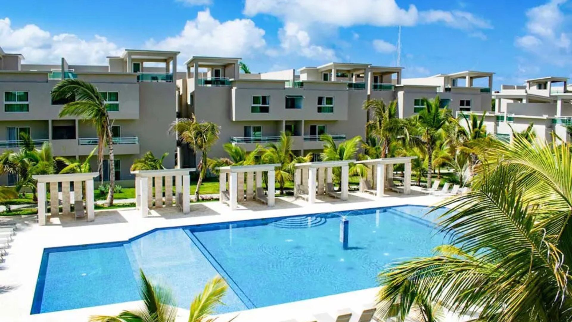 Resort en Punta Cana con piscina al aire libre, palmeras y edificios modernos con balcones.