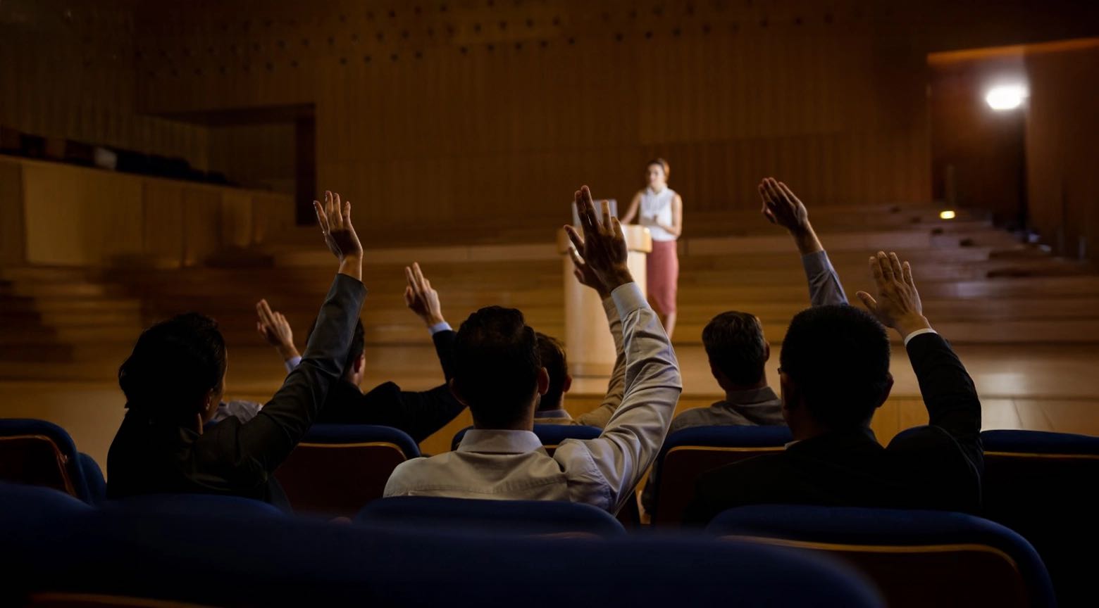 Estudiantes levantan la mano durante una clase en un auditorio educativo.