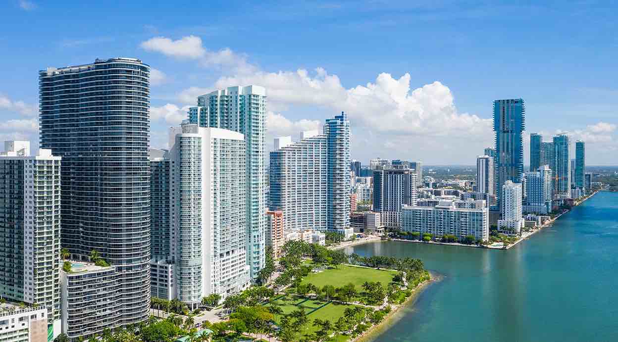 Vista aérea de los rascacielos en Miami, con el océano y áreas verdes en primer plano.