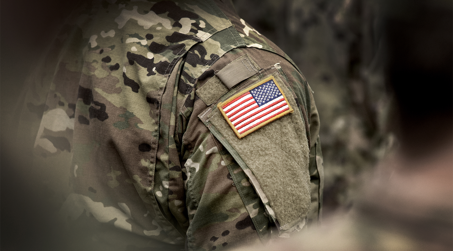 Un soldado con un uniforme camuflaje y una bandera de los Estados Unidos en su hombro.