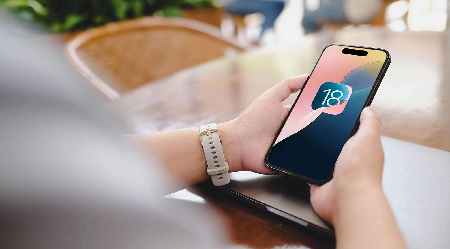 "Un hombre sostiene un iPhone con el logo de iOS 18 en la pantalla, mientras usa una correa de reloj deportiva en su muñeca."