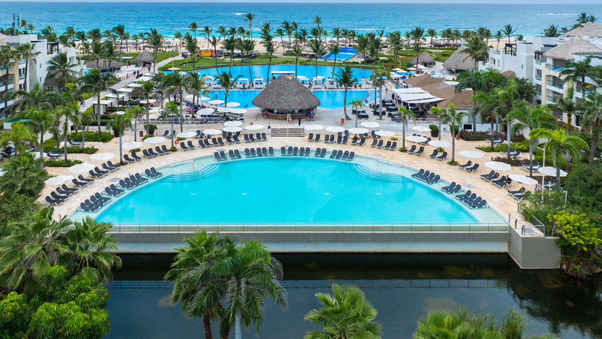 Vista aérea de un complejo hotelero frente a la playa en Punta Cana, con una gran piscina rodeada de tumbonas.