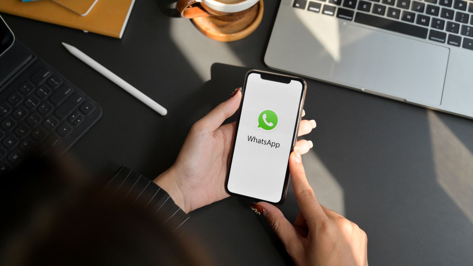 Persona sosteniendo un teléfono con la aplicación WhatsApp abierta sobre un escritorio de trabajo.