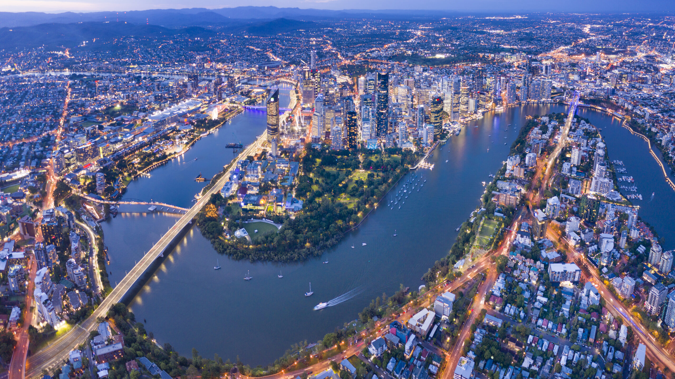 Vista aérea de Brisbane, Australia, con el río Brisbane atravesando la ciudad iluminada al anochecer.