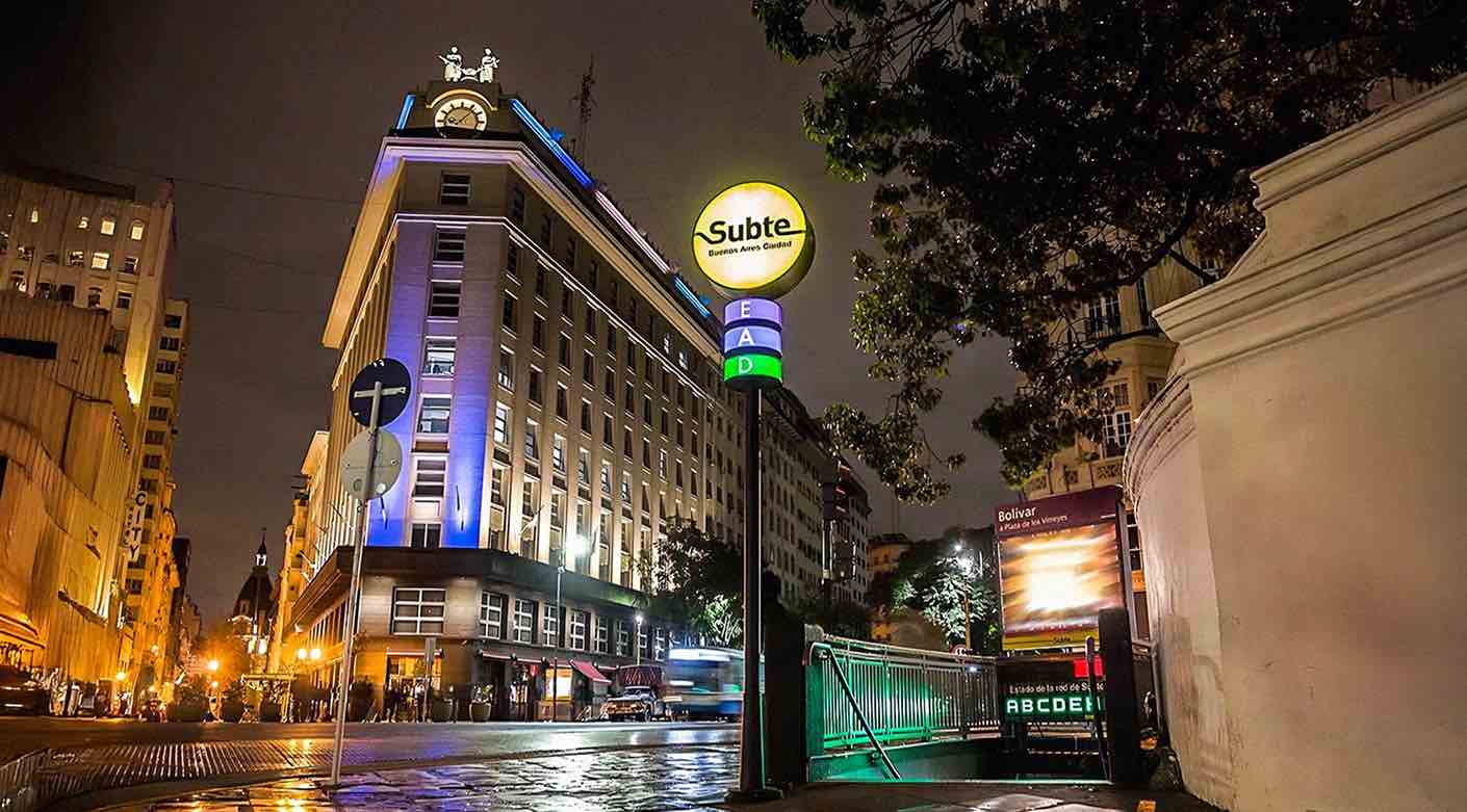 Entrada del metro Subte en Buenos Aires de noche con señal iluminada y edificios alrededor.