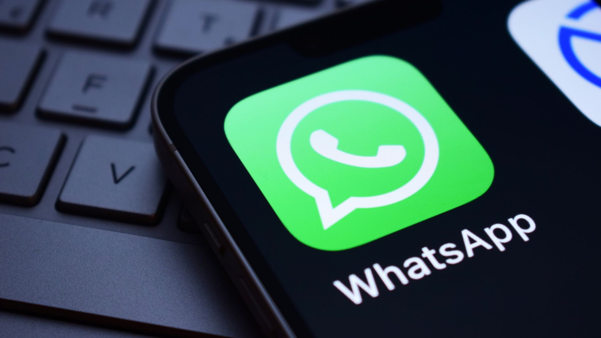 Icono de WhatsApp en una pantalla de teléfono móvil, con el teclado de una computadora de fondo.