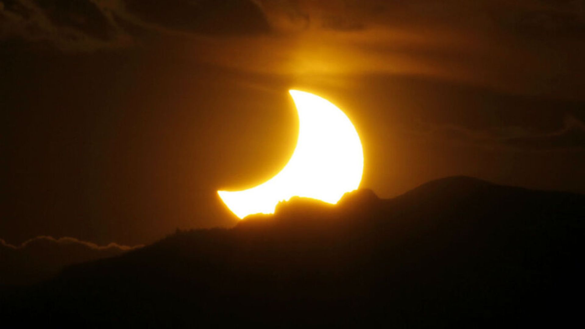 Eclipse solar parcial visible sobre el horizonte con el sol parcialmente cubierto.