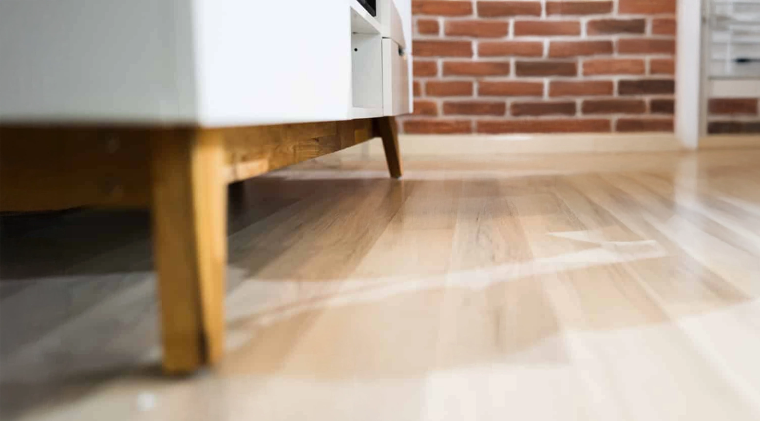 Imagen de un mueble con patas de madera, mostrando el suelo de madera clara y una pared de ladrillos.