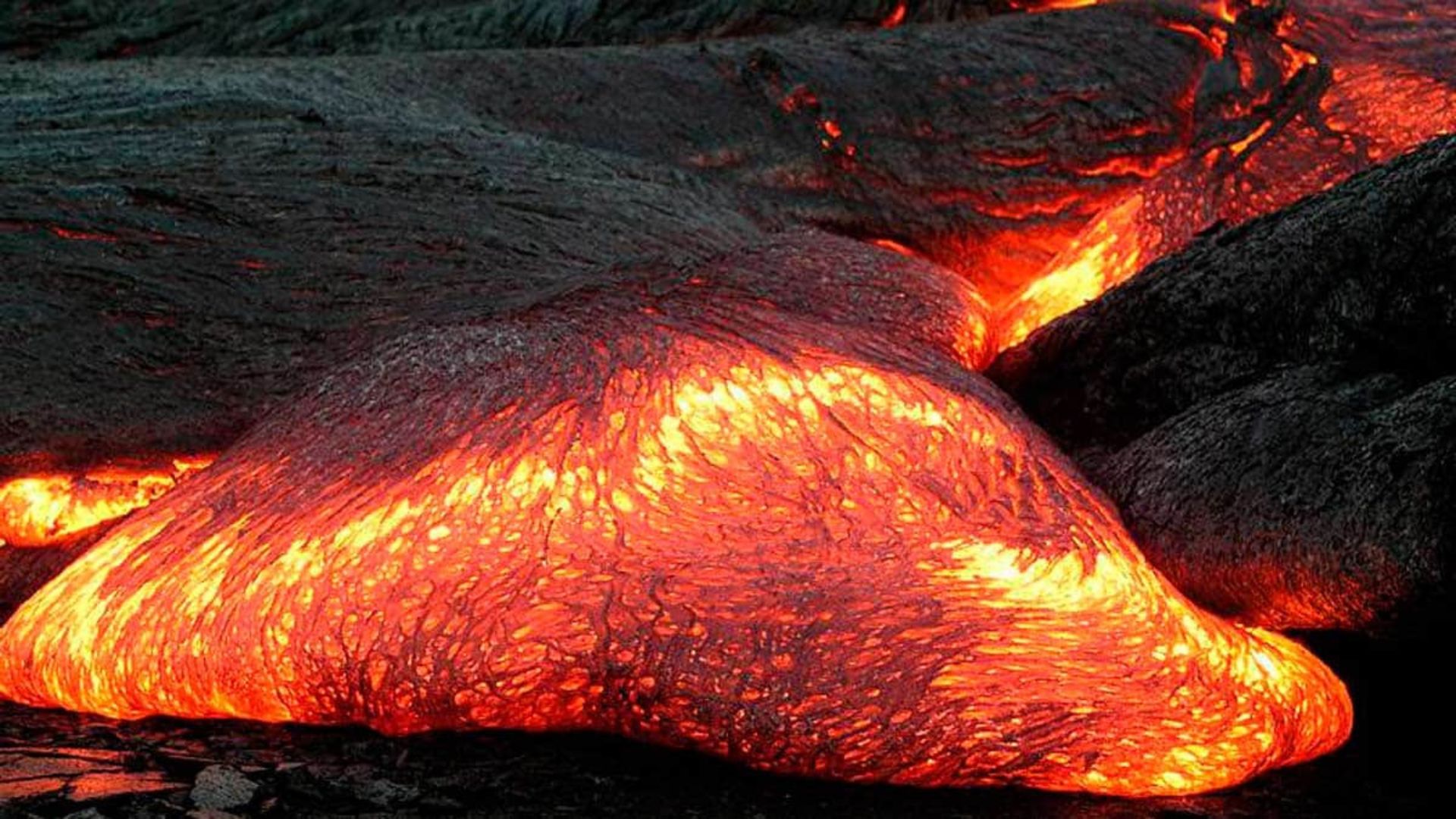 Flujo de lava incandescente avanzando sobre roca volcánica oscura.