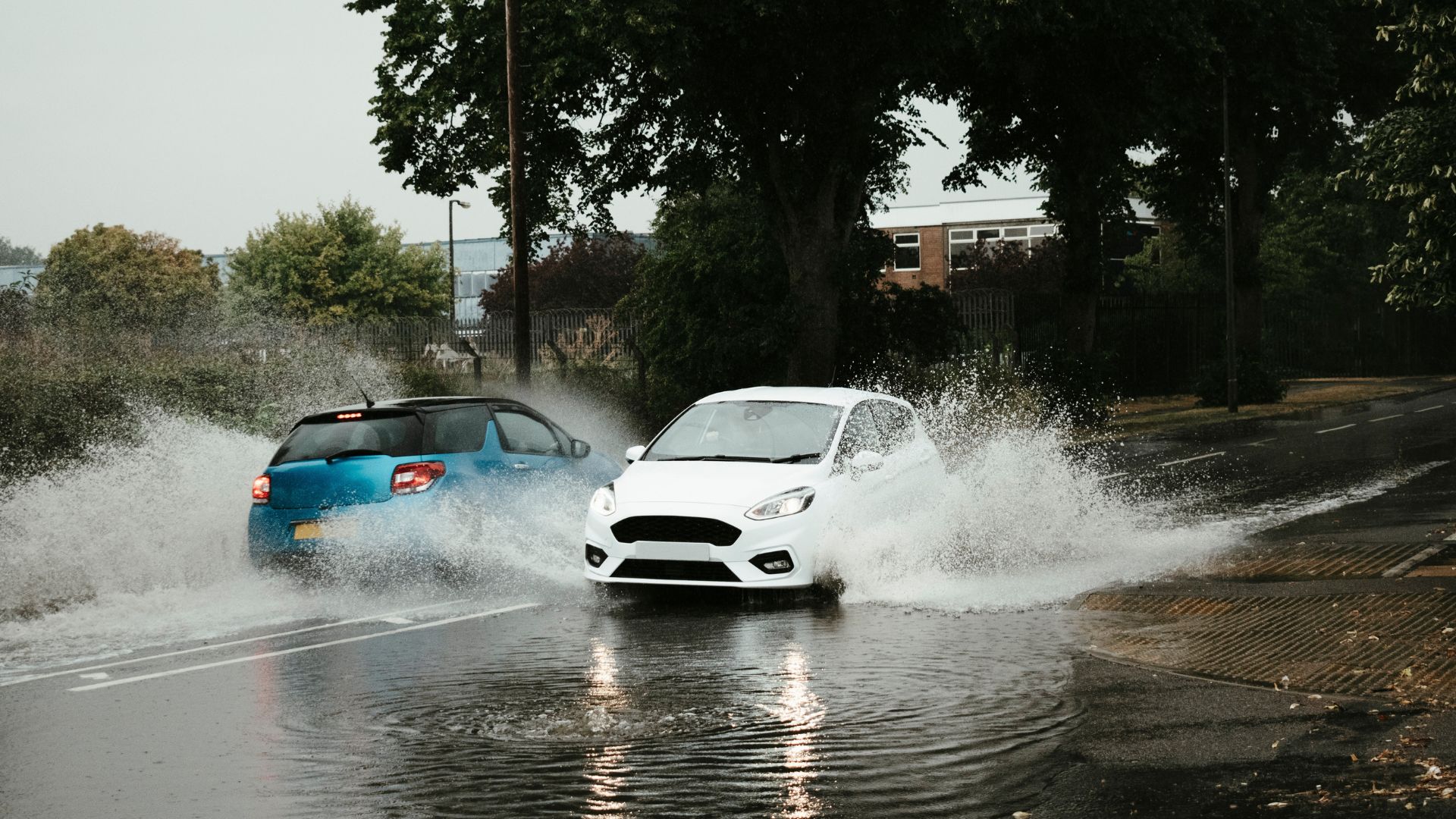 Vehículos circulando por una calle inundada tras fuertes lluvias, levantando agua a su paso.