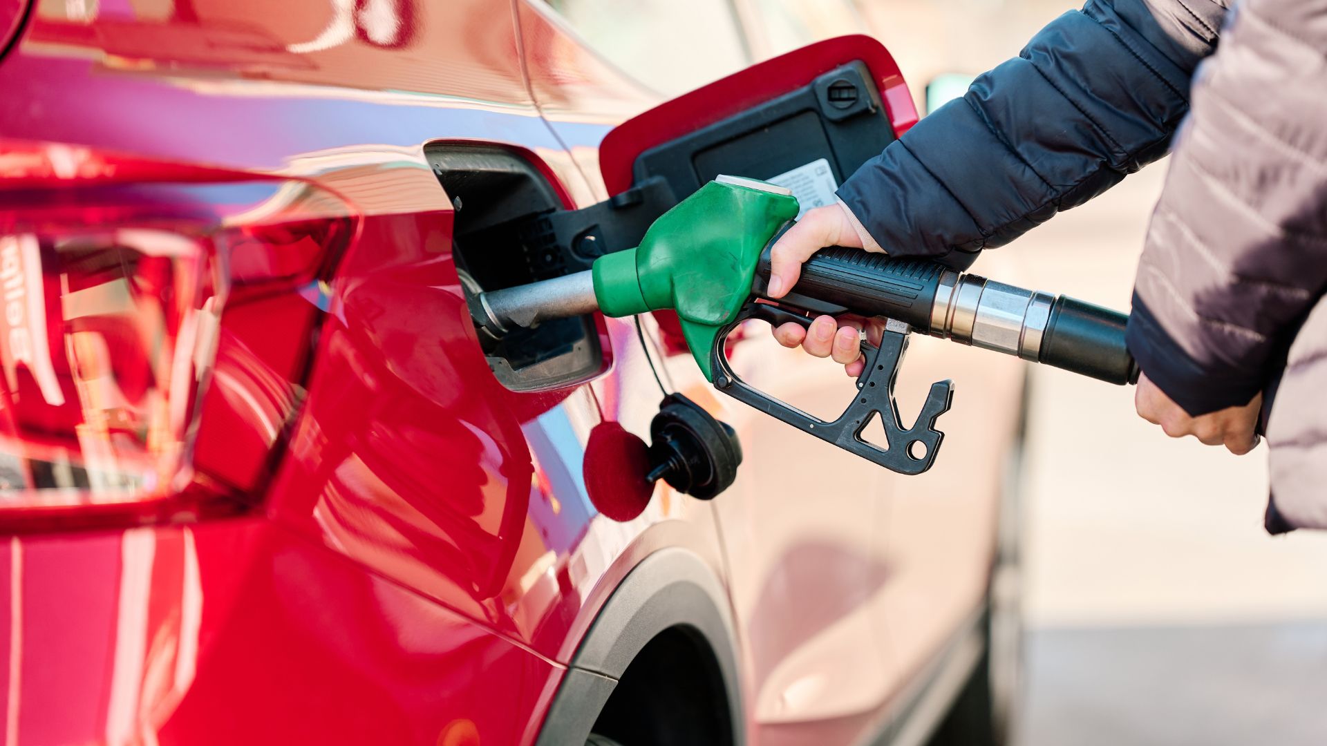 Persona cargando gasolina a un vehículo rojo en una estación de servicio.