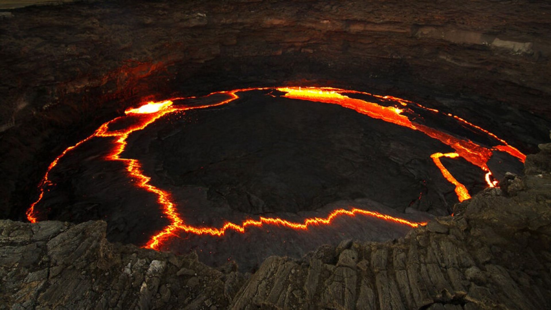 Cráter volcánico con lava incandescente formando un anillo brillante en su interior.