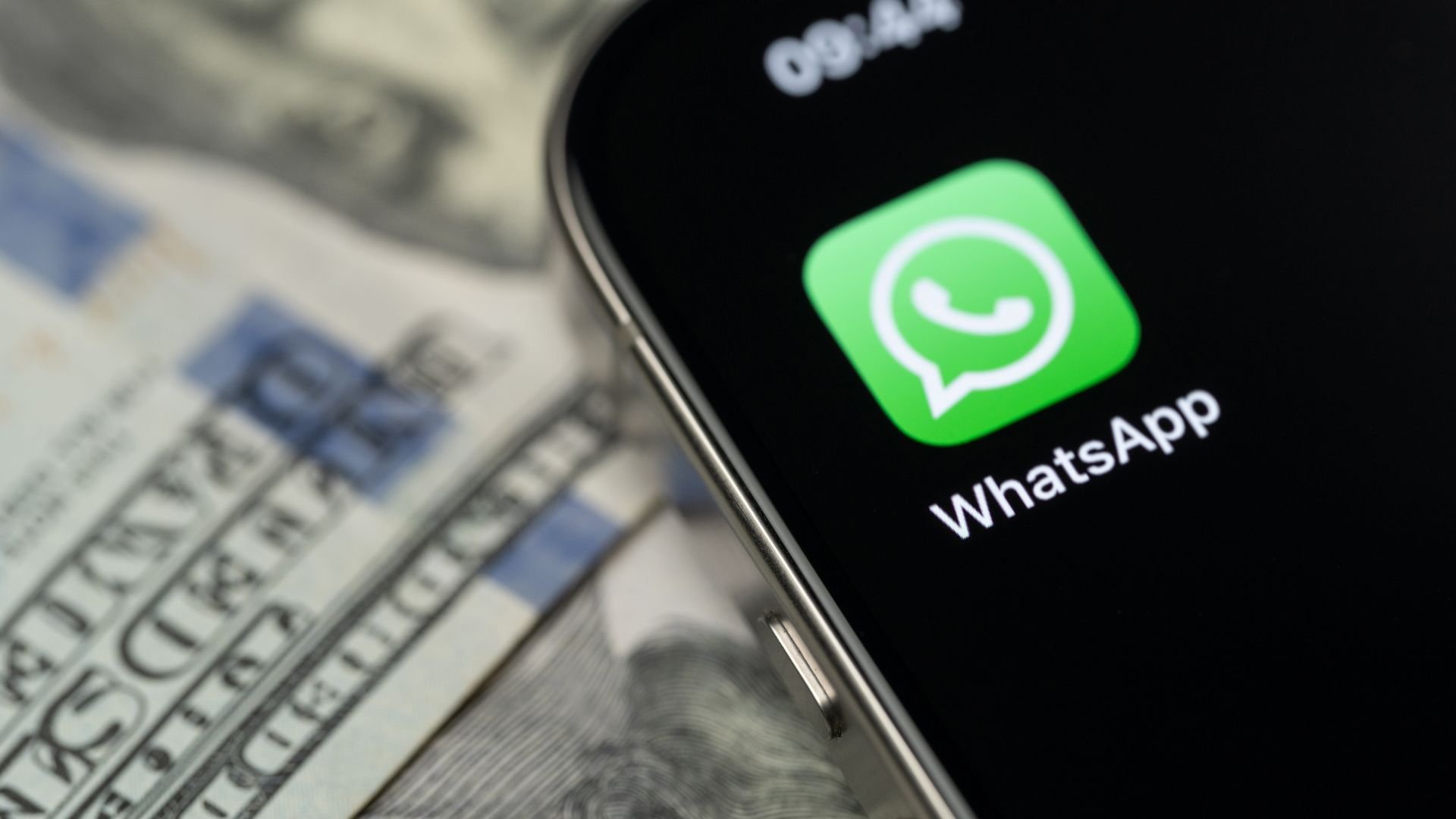 Pantalla de smartphone con la aplicación WhatsApp sobre billetes de dólares.