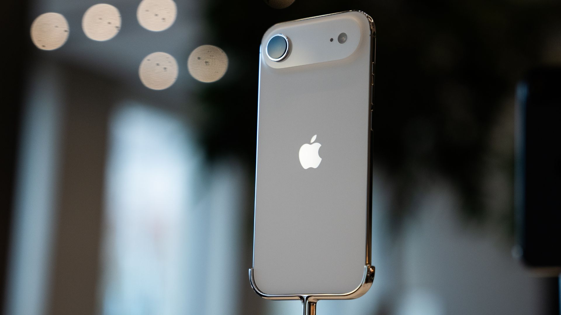 Primer plano de un iPhone blanco con el logo de Apple visible en su parte posterior, con un fondo difuso de luces suaves.