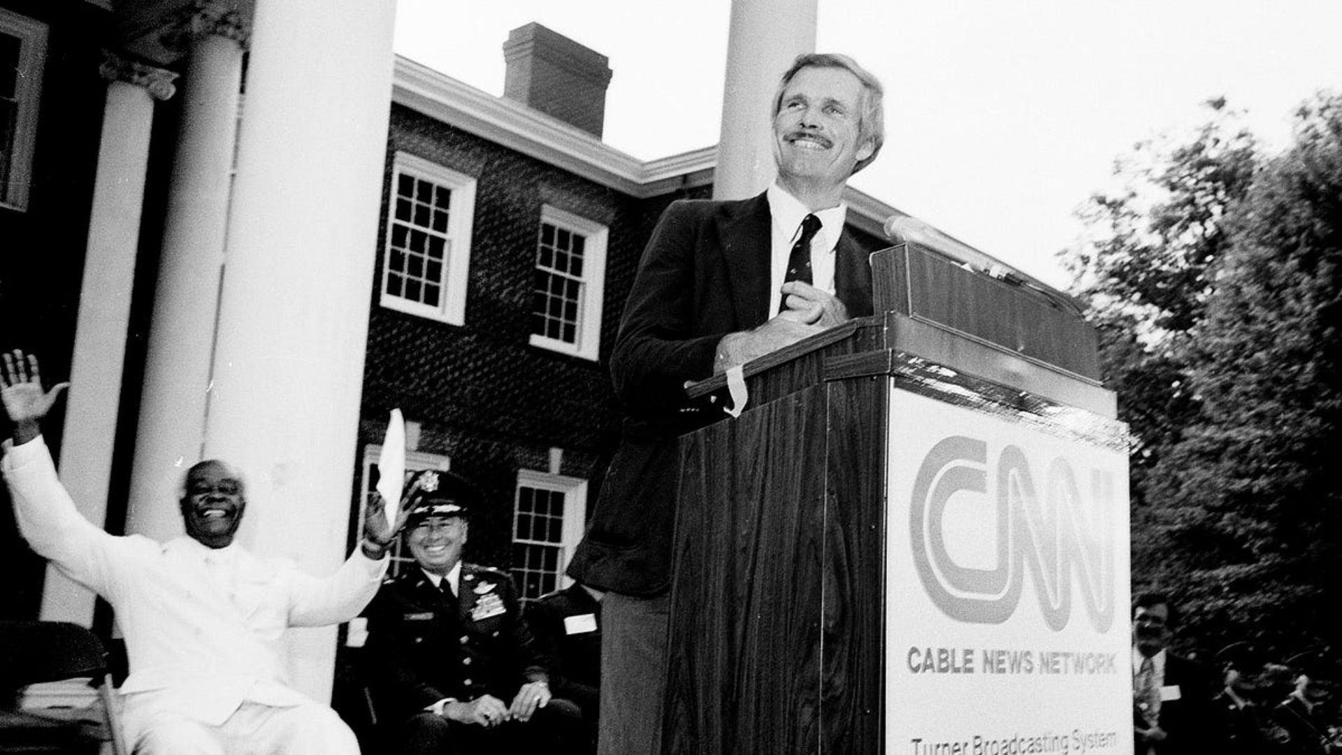 Ted Turner ofrece un discurso frente a un podio con el logotipo de CNN durante un evento institucional.