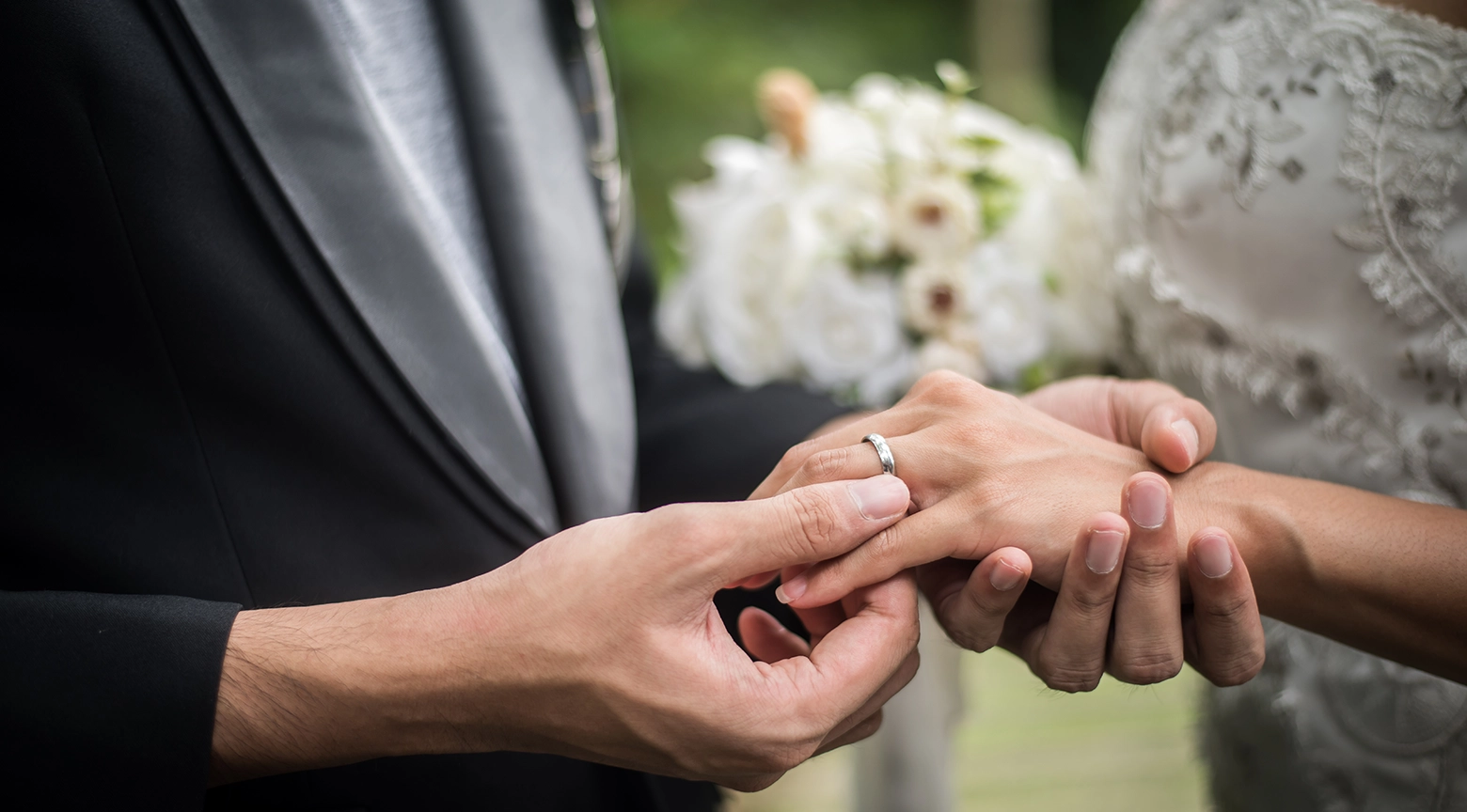 Pareja intercambiando anillos de boda, con foco en las manos del novio colocando el anillo en el dedo de la novia durante la ceremonia nupcial.