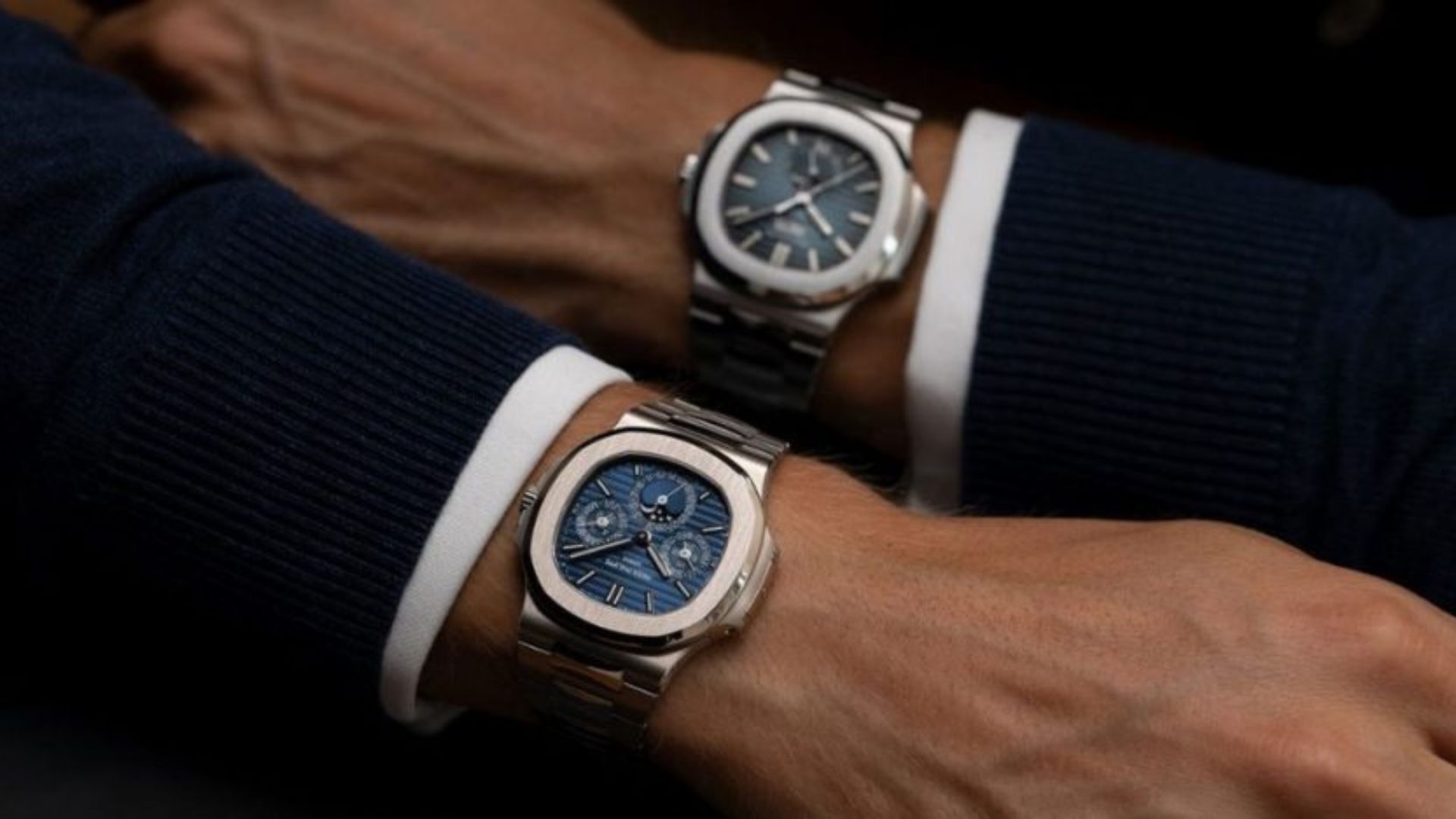 Dos relojes de lujo de acero inoxidable sobre las muñecas de hombres vestidos con trajes oscuros, destacando diseños clásicos de alta relojería.
