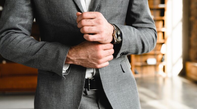 Hombre ajustando la manga de su traje gris mientras luce un reloj de pulsera.
