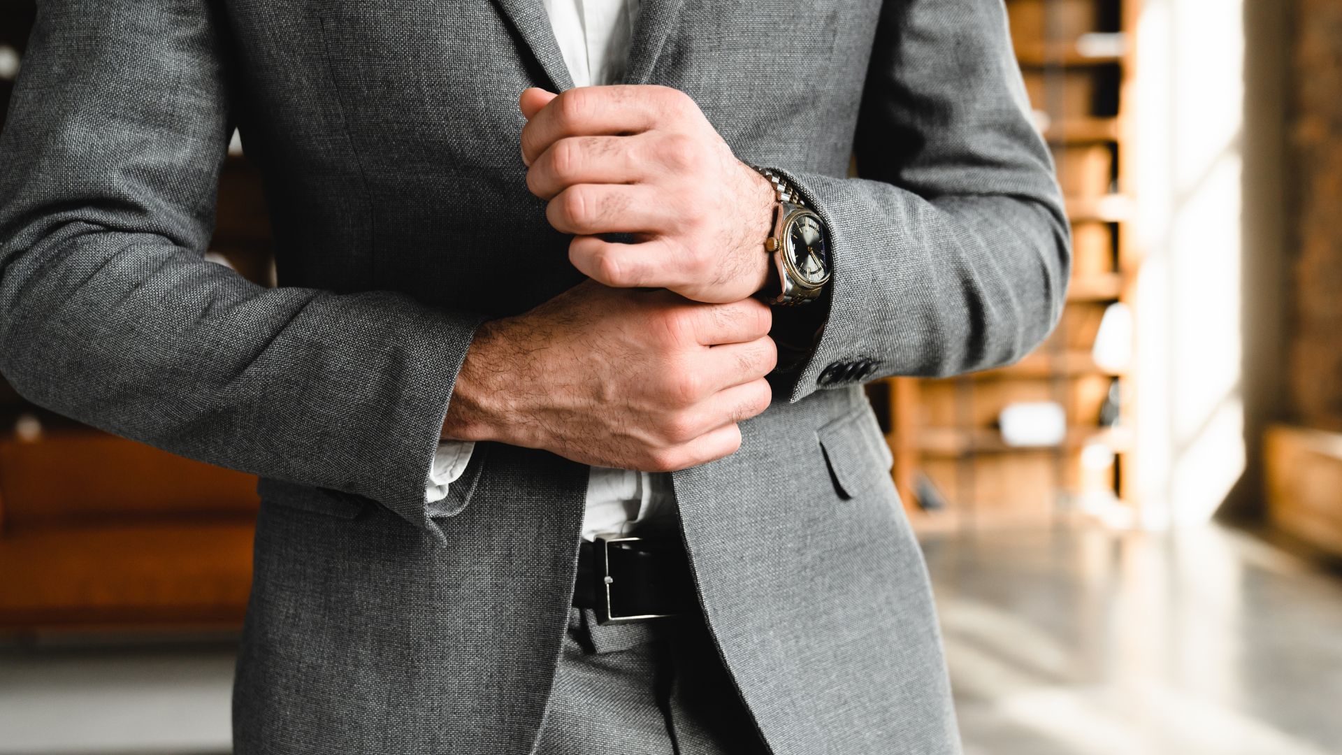 Hombre ajustando la manga de su traje gris mientras luce un reloj de pulsera.
