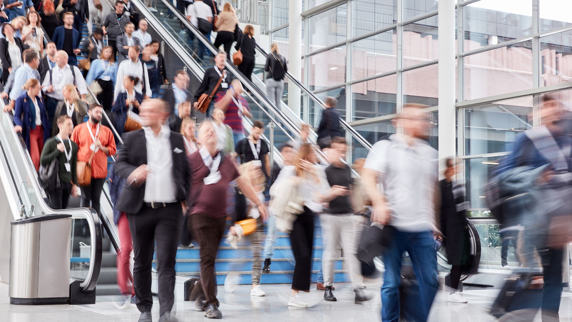 Multitud de personas desplazándose por escaleras mecánicas y pasillos en un concurrido centro de transporte o convención.