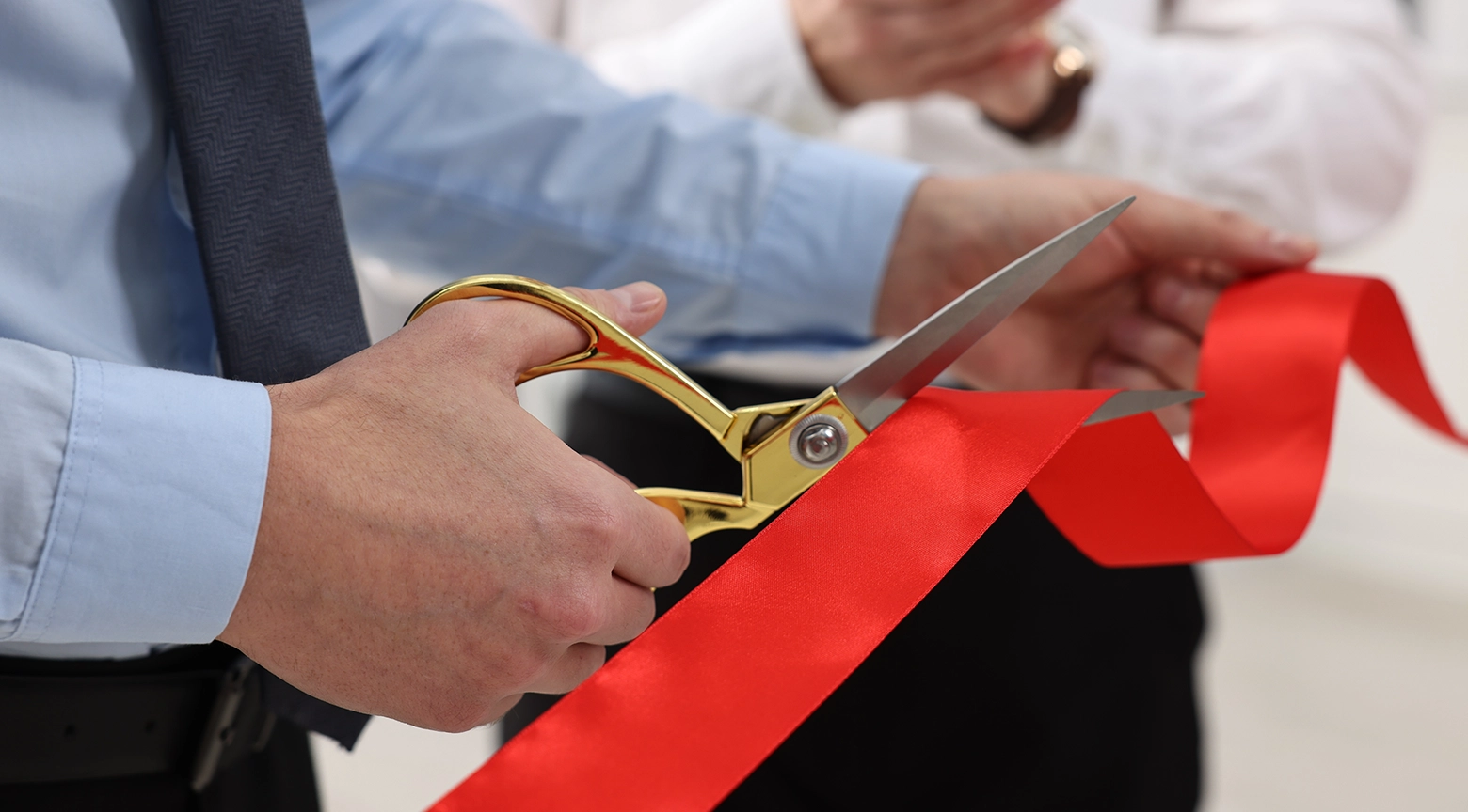 Persona cortando una cinta roja con unas tijeras doradas durante una ceremonia de inauguración o apertura empresarial.