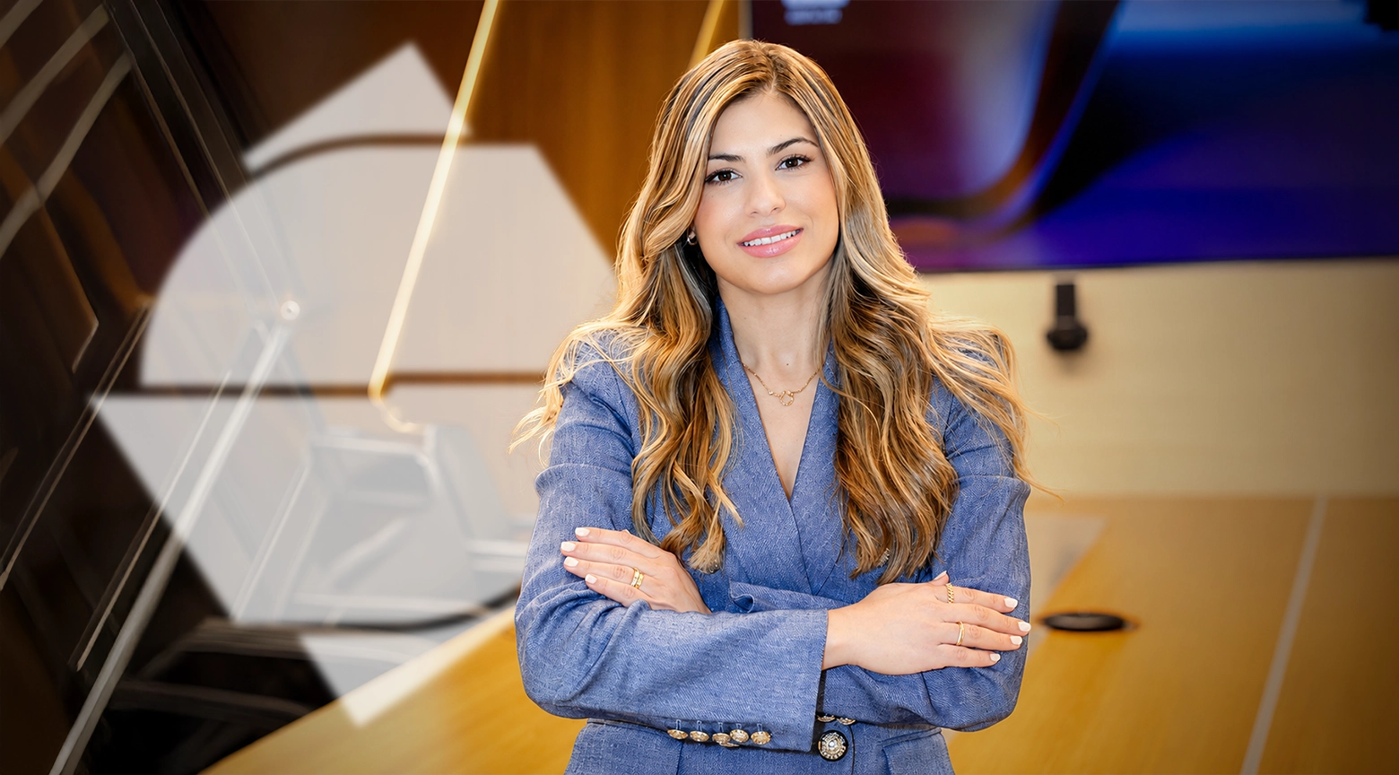 "Mujer profesional de pie con los brazos cruzados en una oficina moderna, con expresión confiada y vestida con blazer azul."