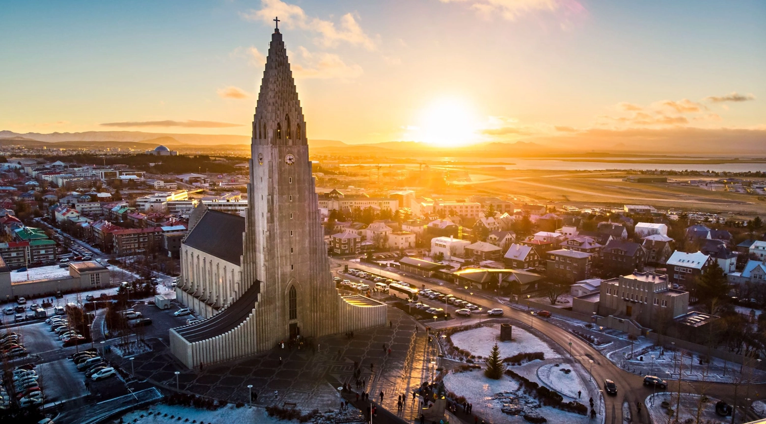 Vista panorámica de Reikiavik, Islandia, al atardecer, con la iglesia Hallgrímskirkja en primer plano, edificios urbanos y un paisaje costero al fondo.