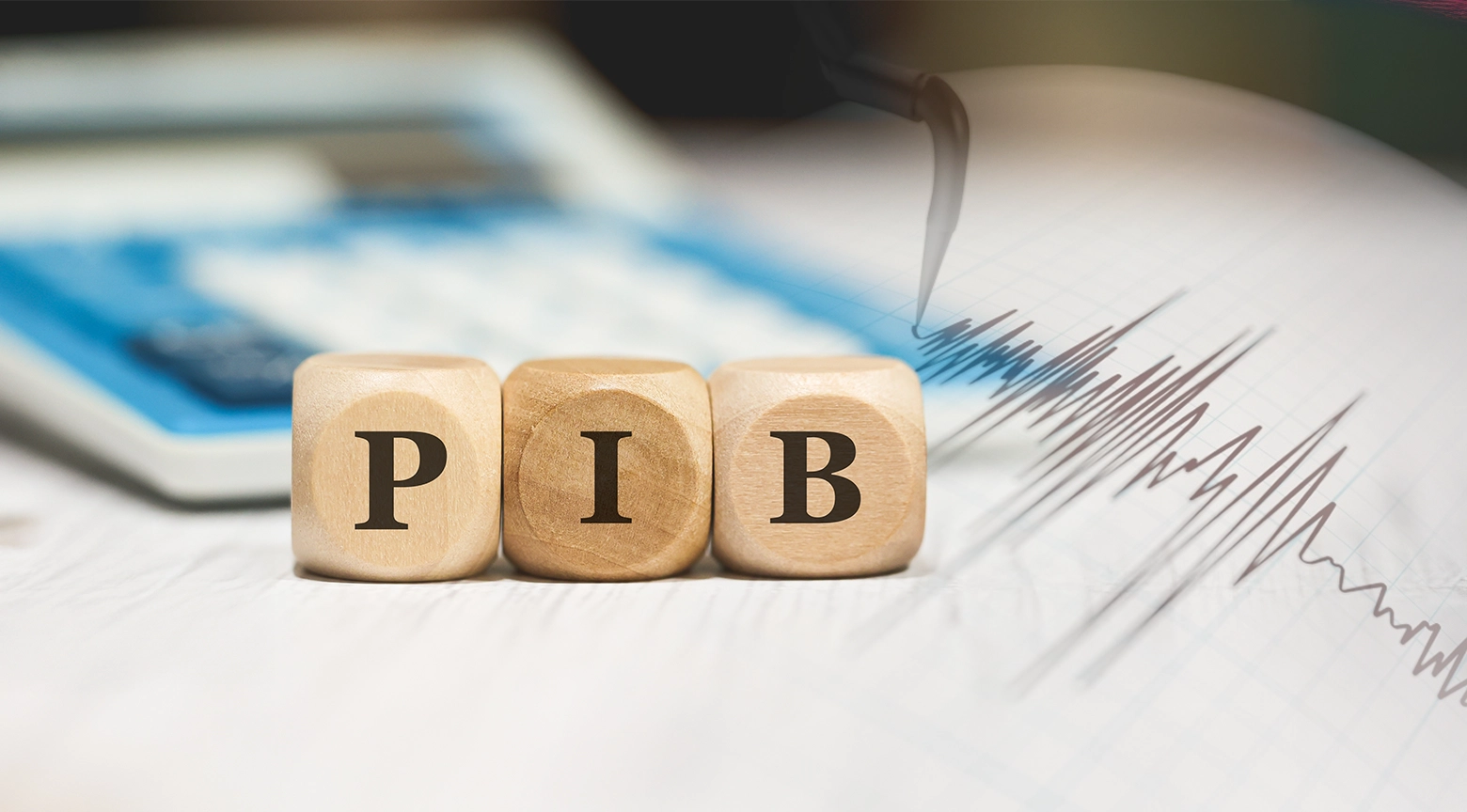 Imagen conceptual de tres cubos de madera con las letras “PIB” sobre documentos financieros, junto a un gráfico de líneas que representa indicadores económicos y posibles variaciones del mercado.