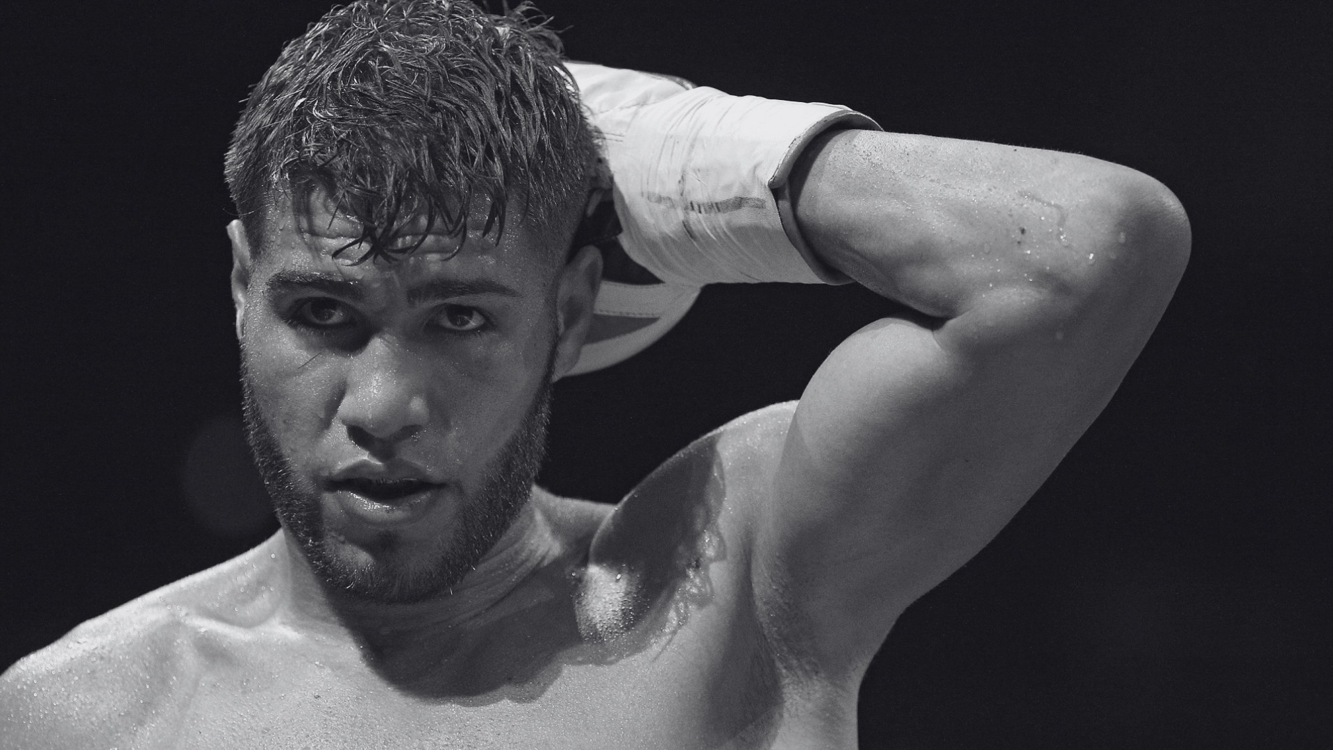 Fotografía en blanco y negro del boxeador puertorriqueño Prichard Colón sobre el cuadrilátero, ajustándose los guantes con expresión pensativa.