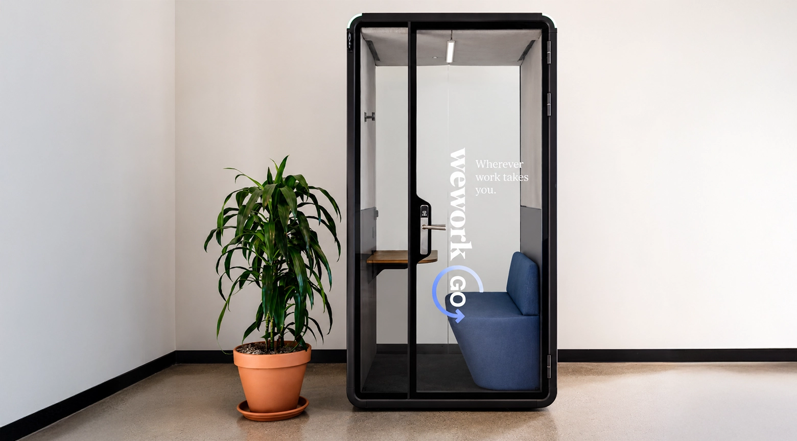 Cabina de oficina privada de vidrio y estructura negra dentro de un espacio de trabajo moderno, con un sillón azul y una planta decorativa al lado.