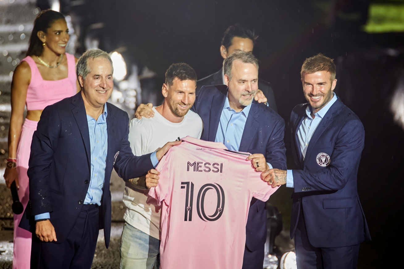Lionel Messi sostiene una camiseta rosa con el número 10 durante su presentación en Inter Miami junto a directivos del club.