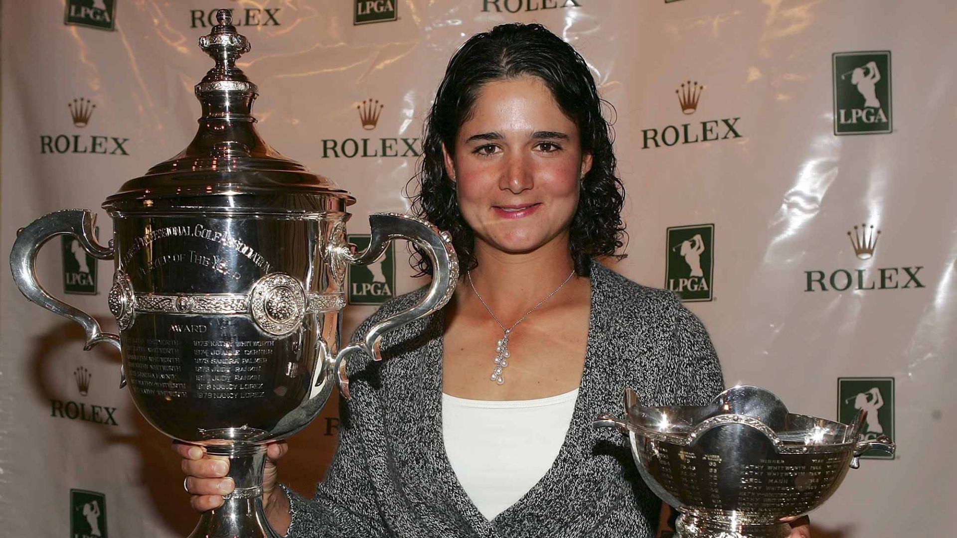 Golfista mexicana junto a dos trofeos de campeonato de golf durante una ceremonia de premiación.