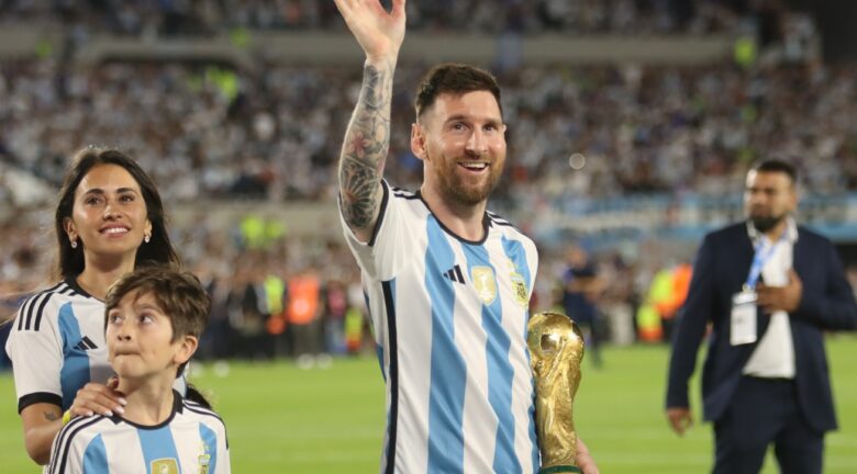 Lionel Messi sostiene el trofeo de la Copa Mundial de la FIFA y saluda desde el campo junto a su familia.