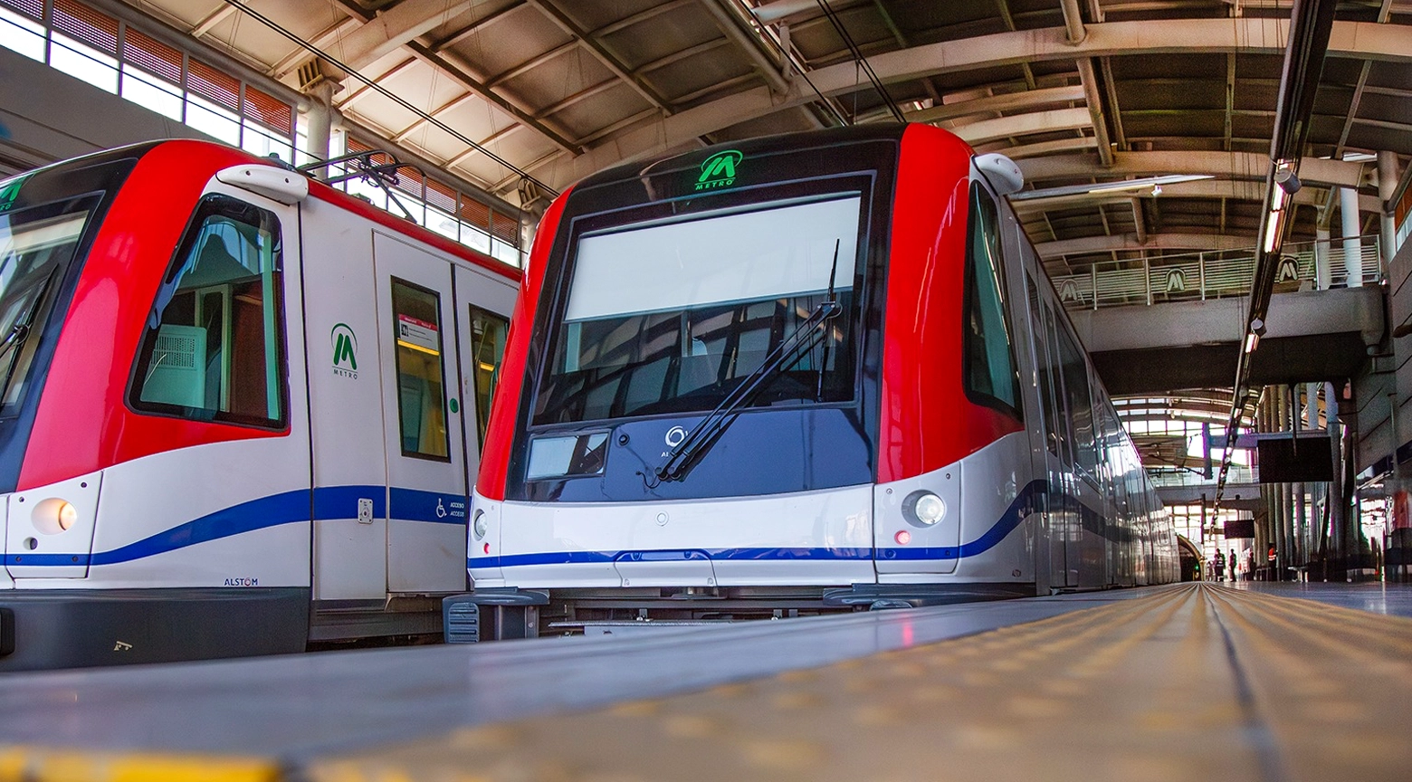 Dos trenes del Metro de Santo Domingo estacionados paralelamente en los rieles de una estación cubierta.