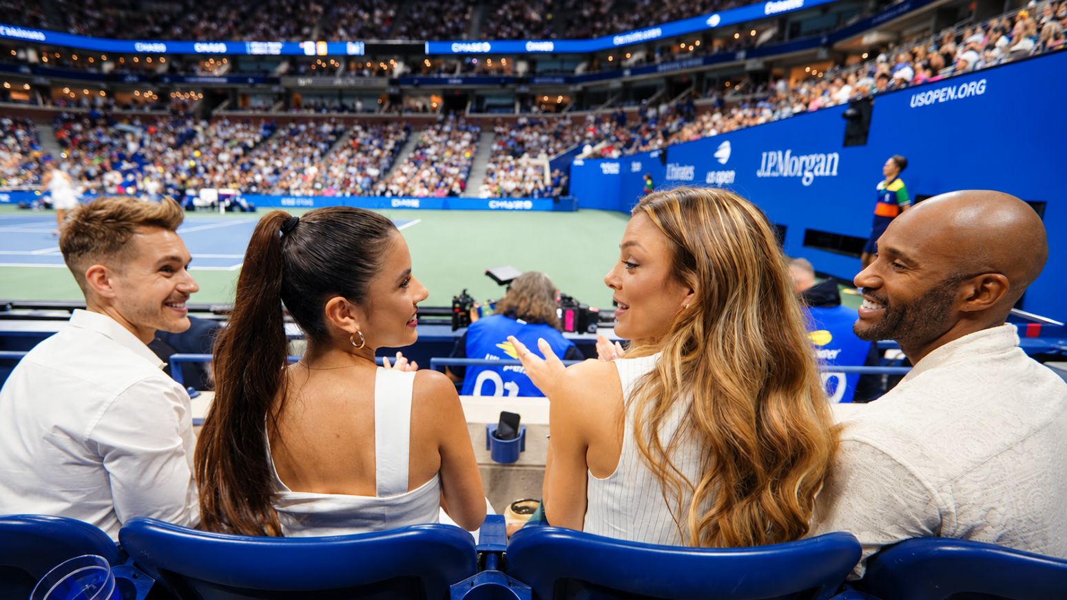 Espectadores conversan desde asientos courtside junto a la cancha del Arthur Ashe Stadium durante el US Open.