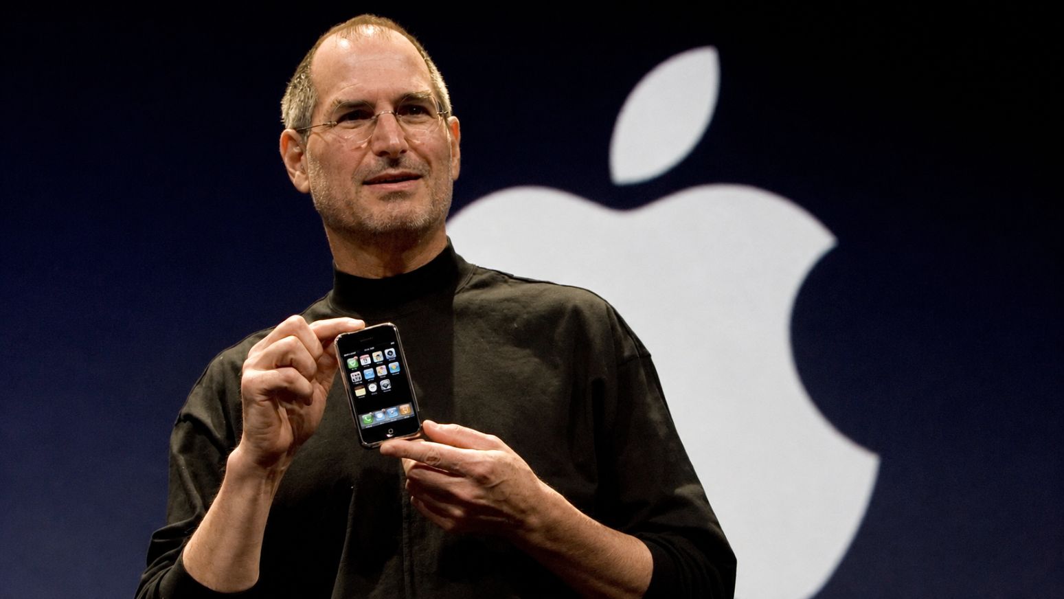 Steve Jobs presenta el primer iPhone en Macworld 2007, sosteniendo el dispositivo frente al logotipo de Apple.