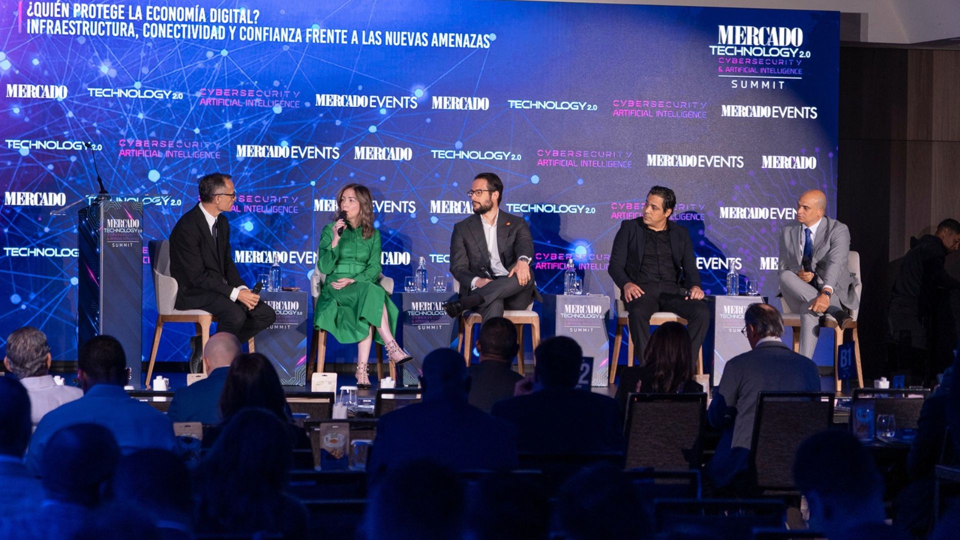 Cinco especialistas participan en un panel sobre ciberseguridad, conectividad y economía digital durante el Mercado Technology 2.0 Summit. Una mujer vestida de verde interviene con un micrófono ante los demás panelistas y el público.