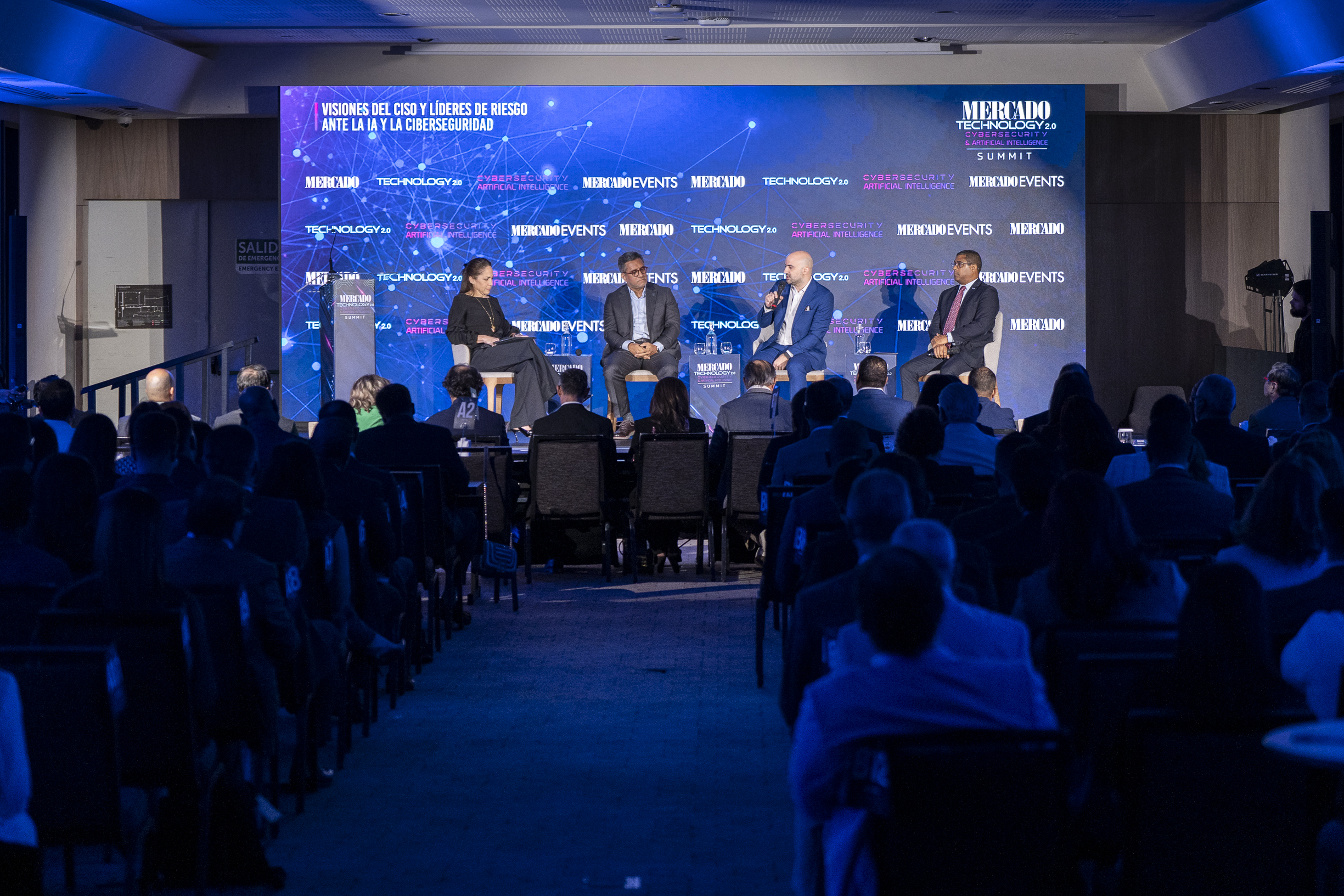 Panel de expertos ante un público en un evento sobre inteligencia artificial y ciberseguridad, con una gran pantalla de fondo que muestra gráficos tecnológicos y la identidad de Mercado Technology 2.0.