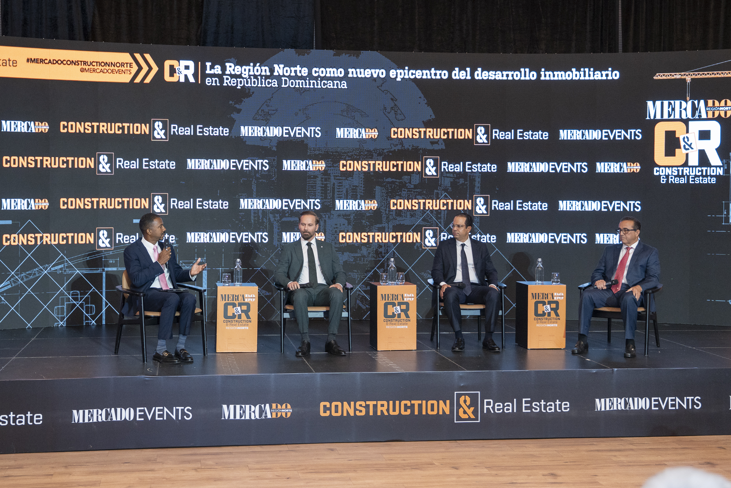 Panel de cuatro especialistas en un escenario de evento sobre el desarrollo inmobiliario de la región norte de República Dominicana, con una pantalla de fondo que anuncia el tema del crecimiento inmobiliario.