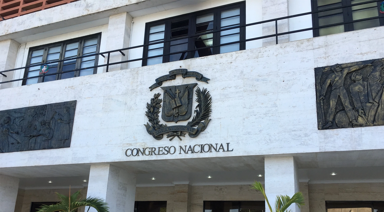 Fachada del Congreso Nacional de República Dominicana, con el escudo nacional en el centro, el nombre de la institución y relieves históricos a ambos lados de la entrada principal.