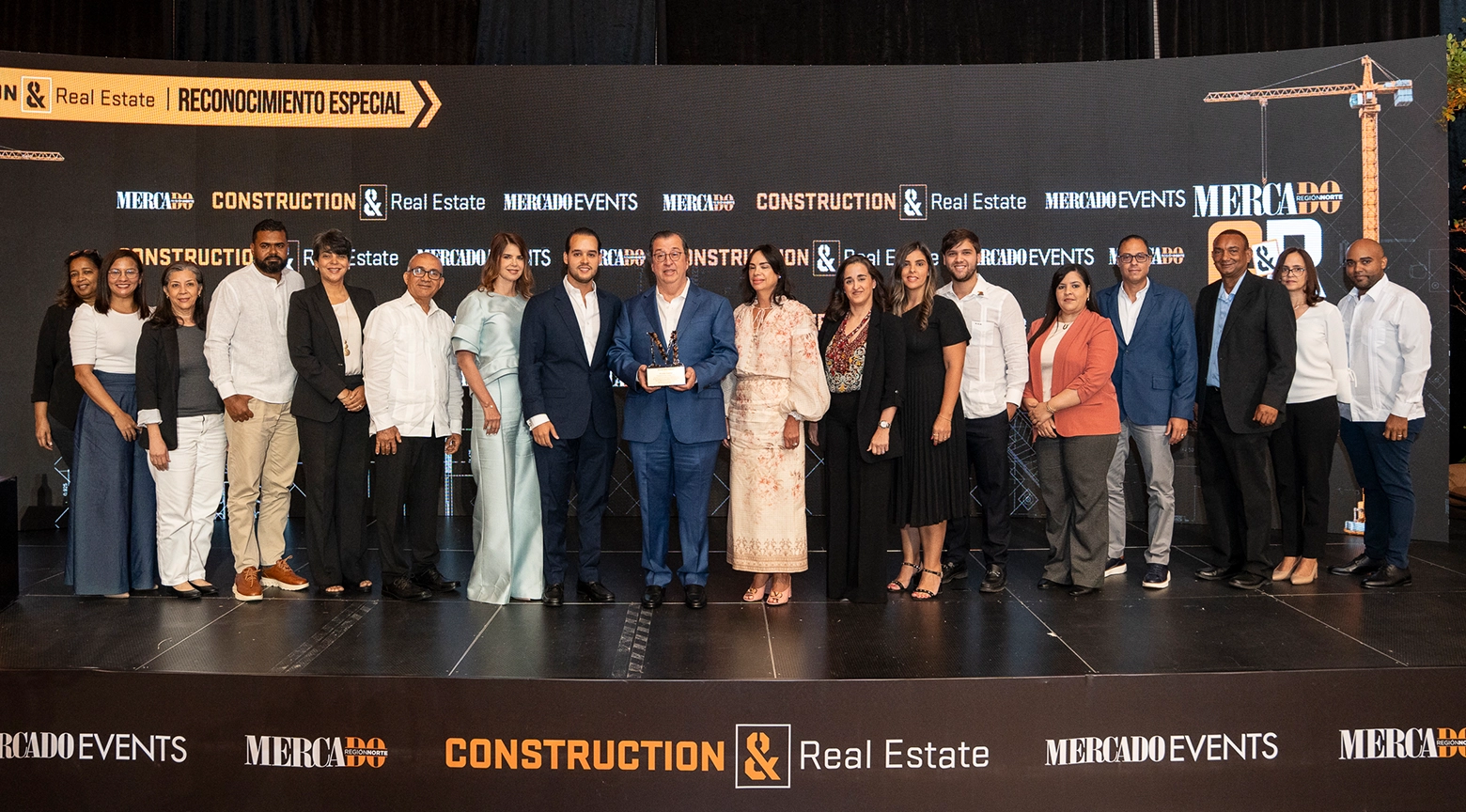 Grupo de profesionales posa en un escenario durante un acto de reconocimiento especial de Mercado Construction & Real Estate, con un premio al centro.