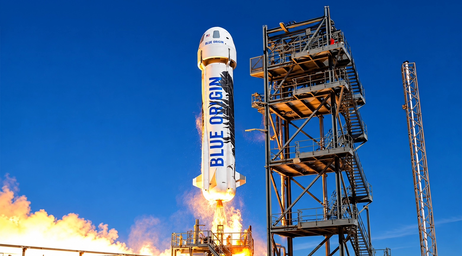 Cohete de Blue Origin despegando verticalmente desde una plataforma de lanzamiento, con llamas y gases expulsados por sus motores. A su derecha se observa una torre metálica de servicio bajo un cielo azul despejado.